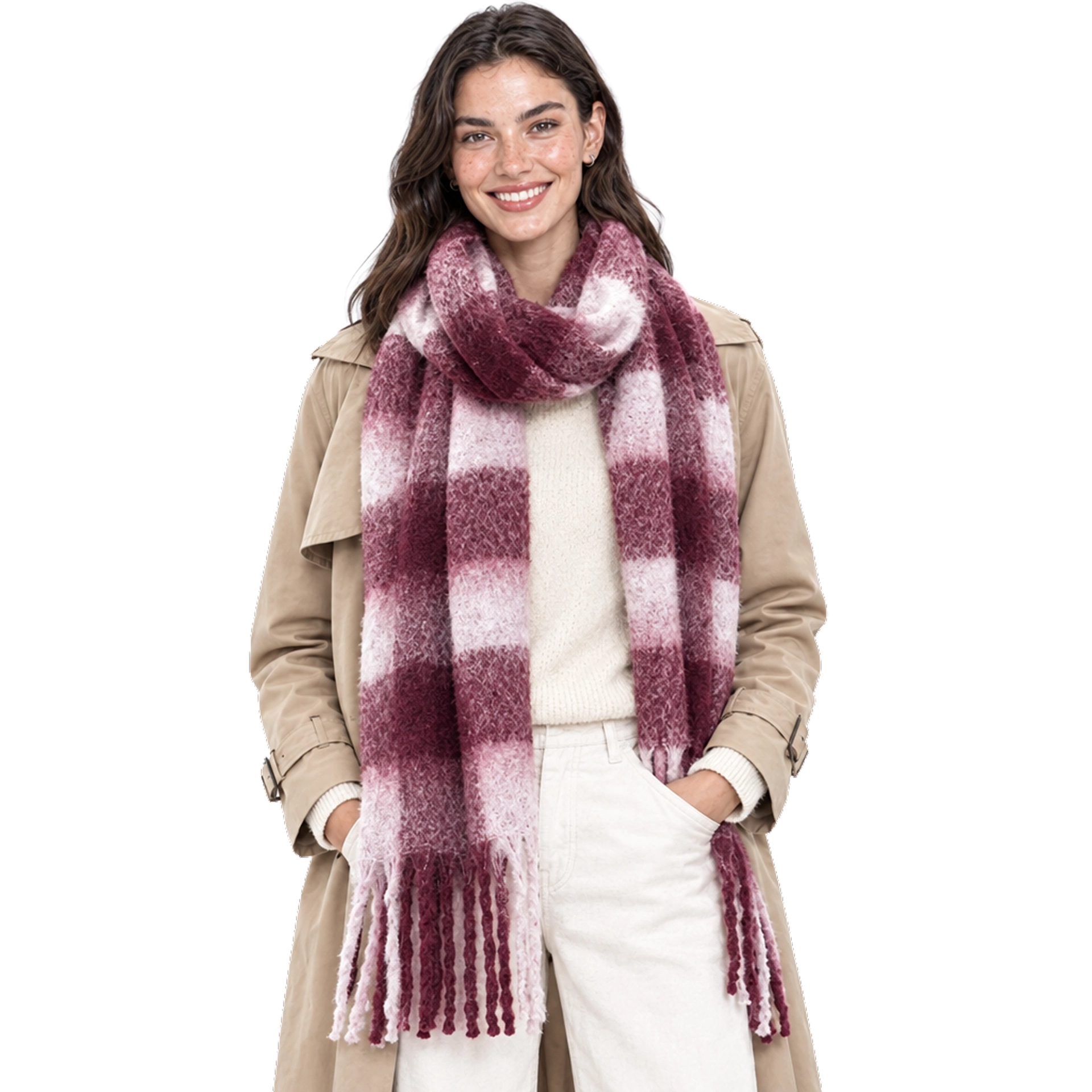 Smiling model with hands in her pockets wearing a Summer & Rose chunky burgundy and pink plaid fringed scarf over a tan trench coat, cream sweater, and cream pants, on a white background.