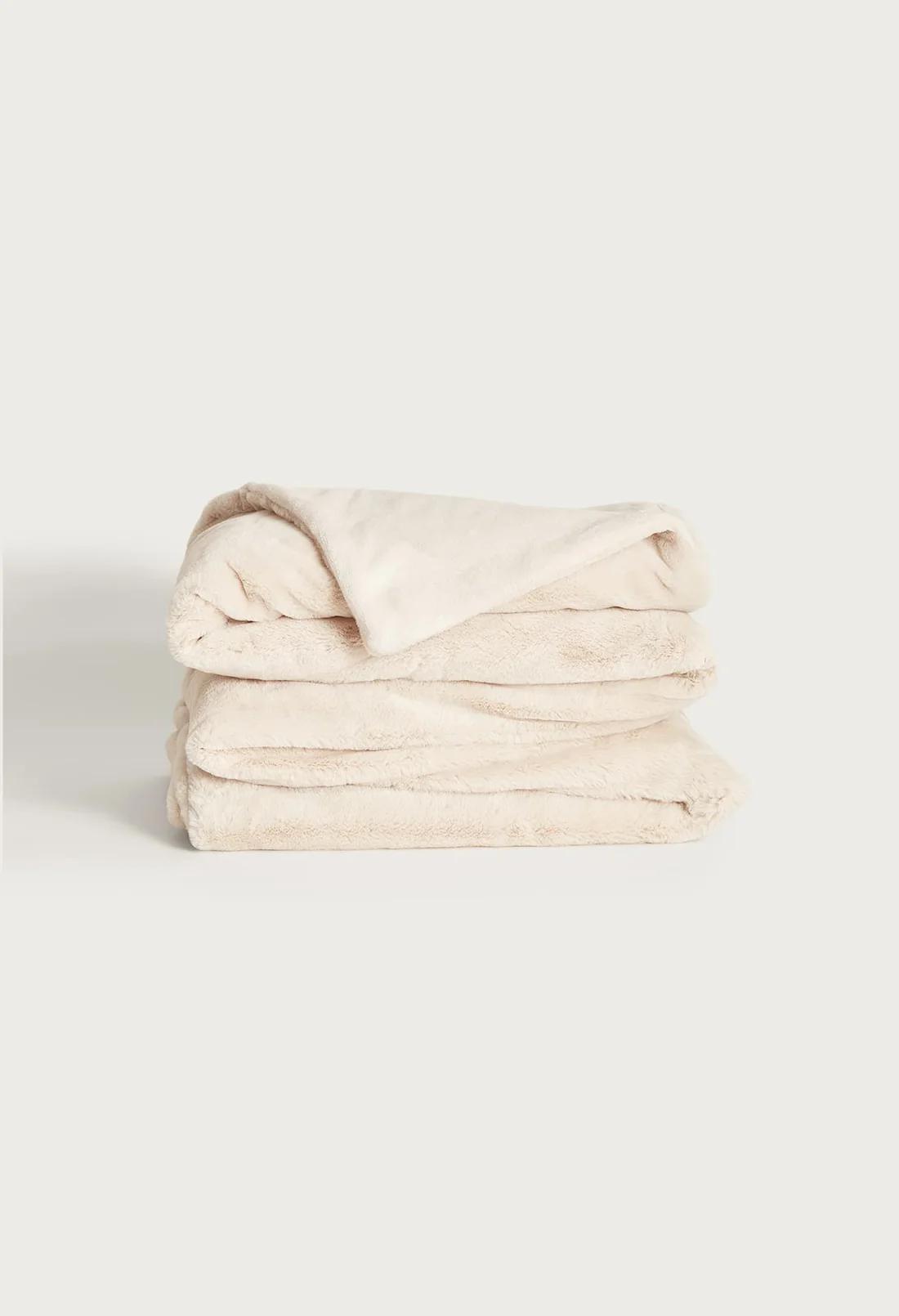 Folded UnHide Cuddle Puddle faux fur blanket in soft cream, stacked in layers with one corner turned back to show the smooth reverse side, against a light background.