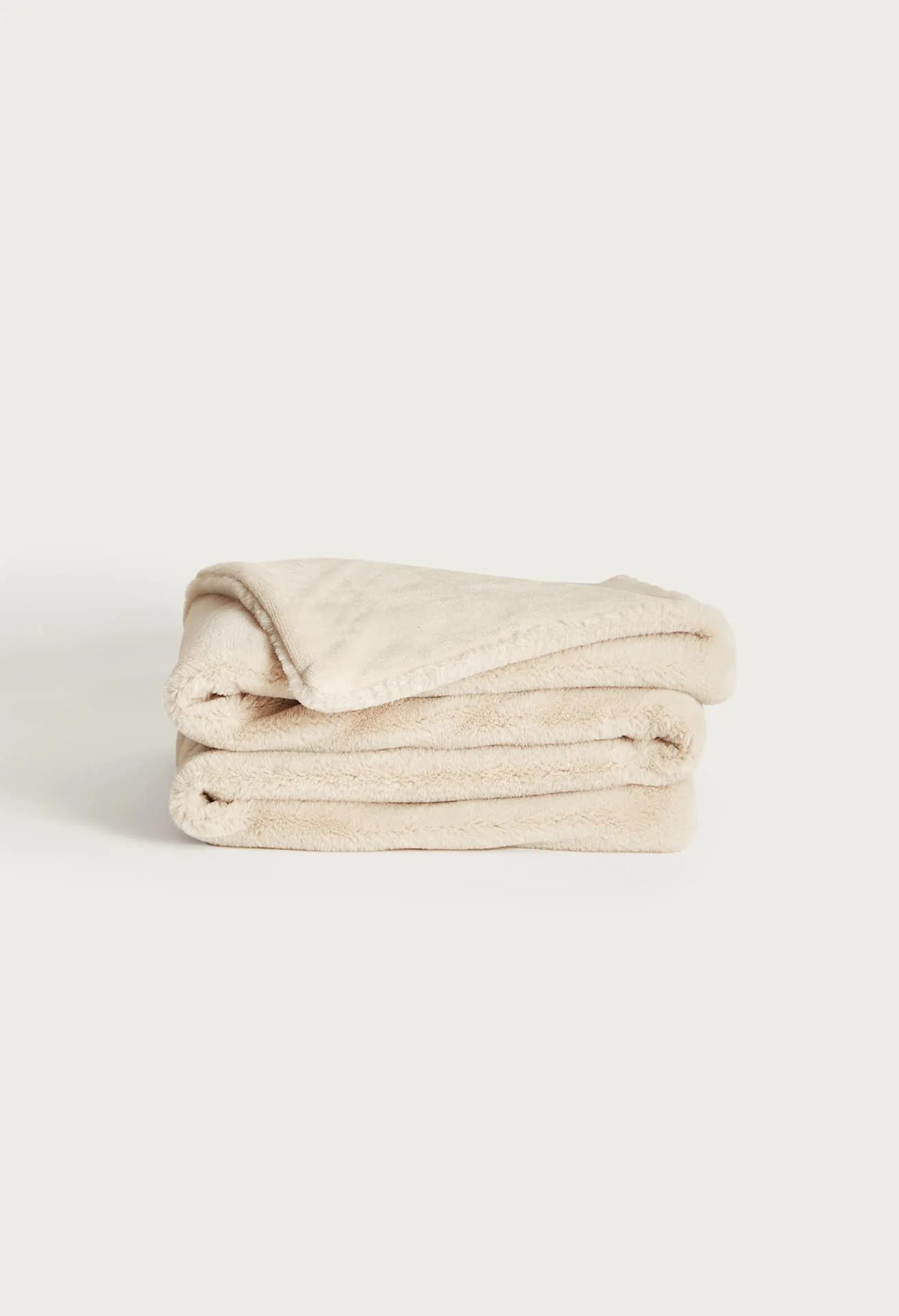 Folded UnHide Lil' Marsh faux fur blanket in cream, stacked in neat layers against a light background.