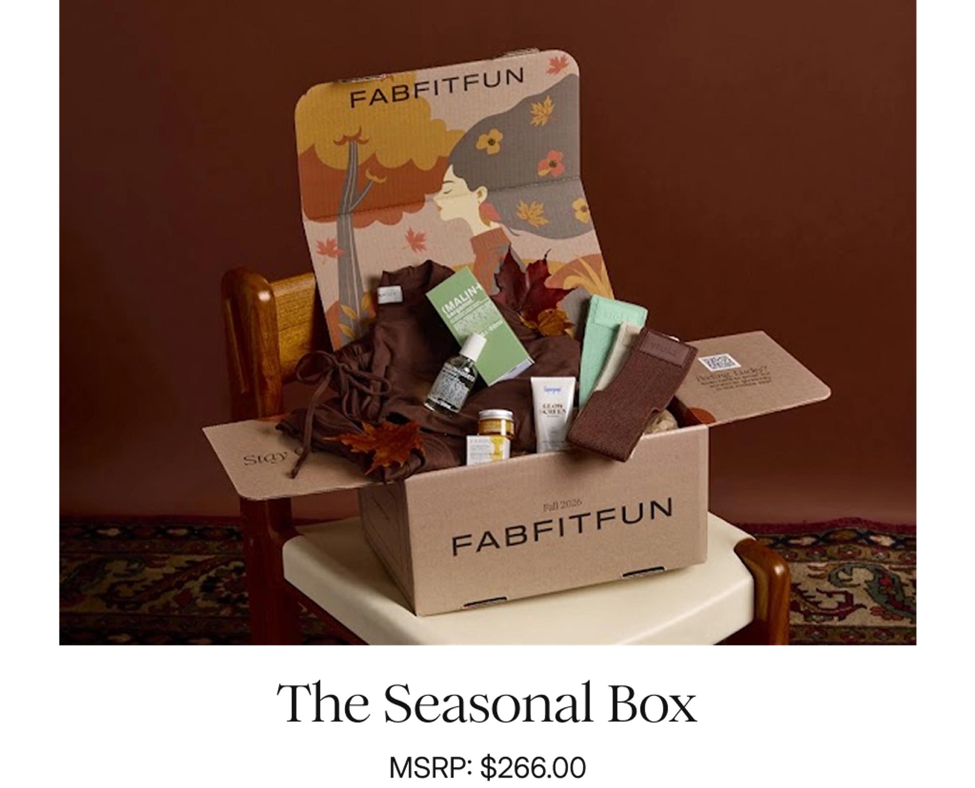 FabFitFun Fall 2026 Seasonal Box open on a wooden chair atop a patterned rug, with an autumn illustration on the lid and products spilling out, including a brown loungewear set, a Malin+Goetz box, skincare bottles, a sunscreen tube, and mint and brown socks, with the caption "The Seasonal Box, MSRP: $266.00."